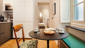 A compact kitchen with modern appliances, a dining area with a round table and bench, and a view of a bedroom through an open door. - Corvetto Luxury Suite by Wonderful Italy (Genoa)