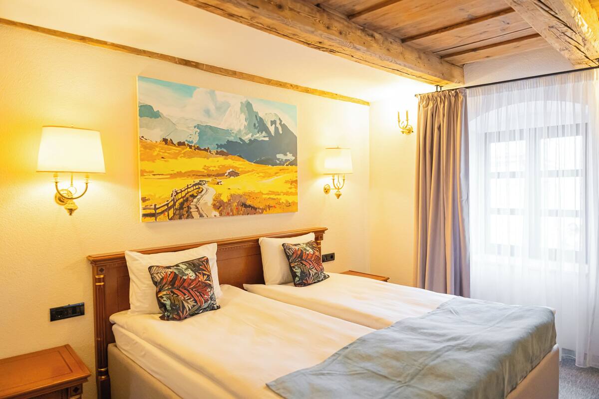 Habitación de hotel con dos camas, un cuadro en la pared y dos lámparas de pared.