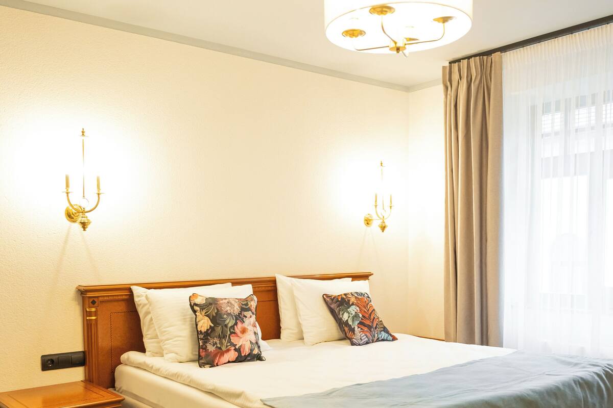 Una cama bien hecha con cabecera de madera, una mesita de noche y una lámpara fijada a la pared.