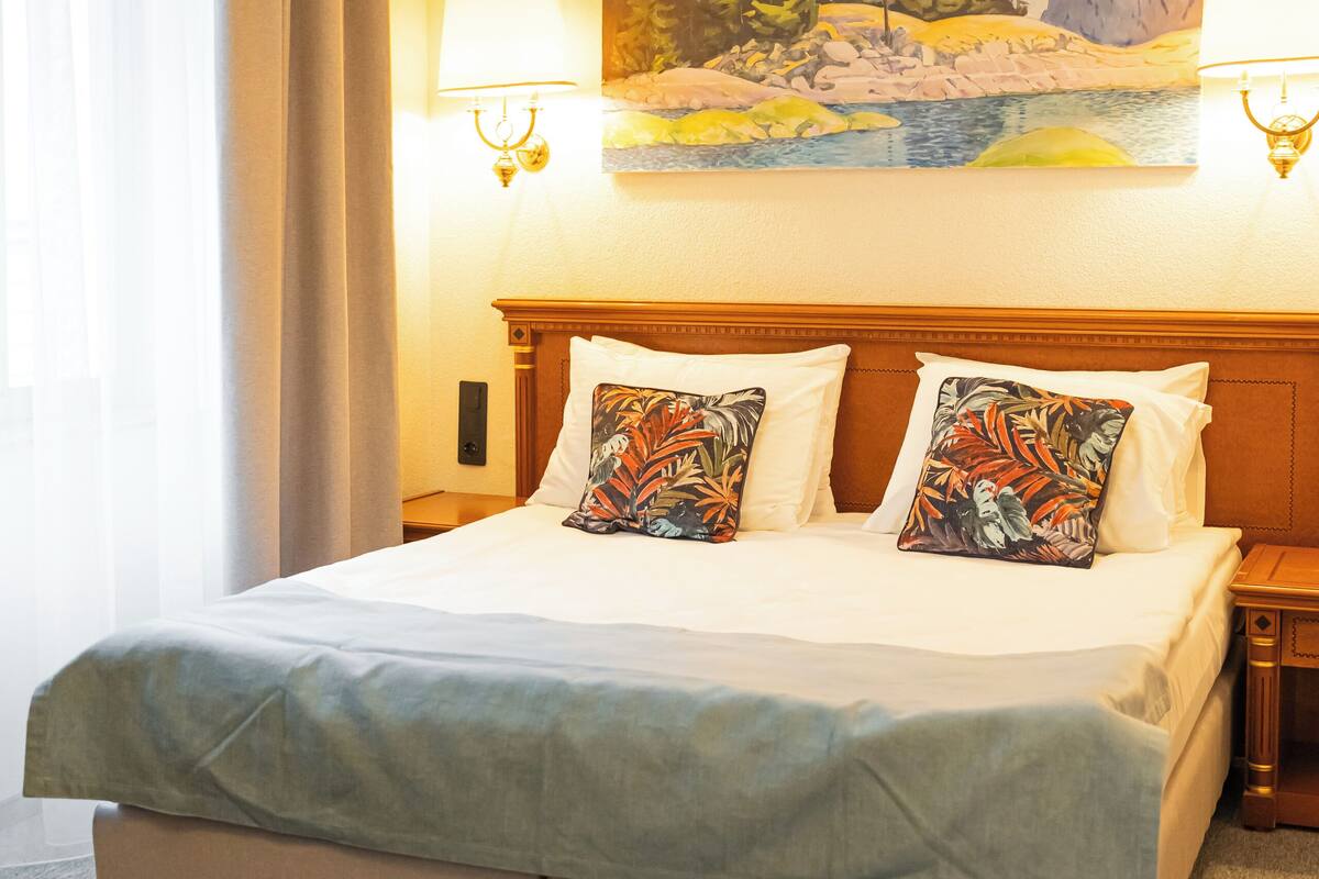 Habitación de hotel con una cama grande, dos almohadas, un cuadro en la pared y una lámpara a cada lado de la cama.