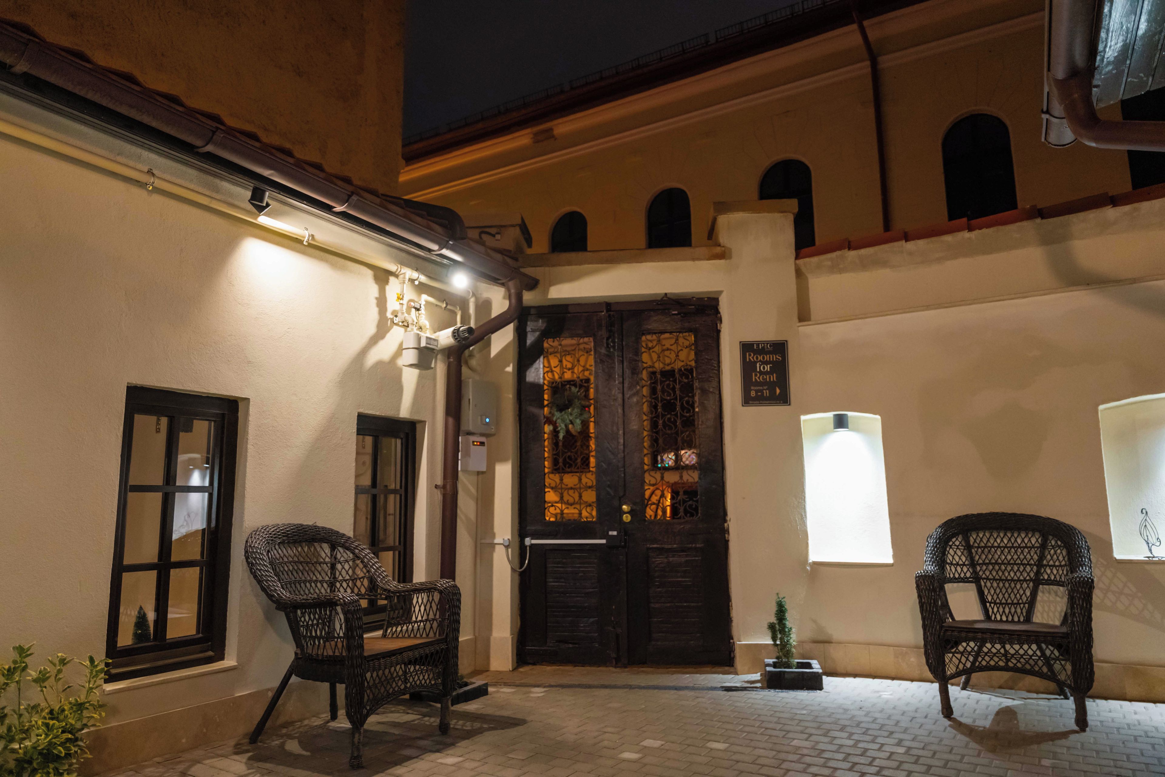 A building entrance with two wicker chairs outside, a door with decorative glass, and a sign indicating rooms for rent.