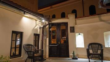 A building entrance with two wicker chairs outside, a door with decorative glass, and a sign indicating rooms for rent.