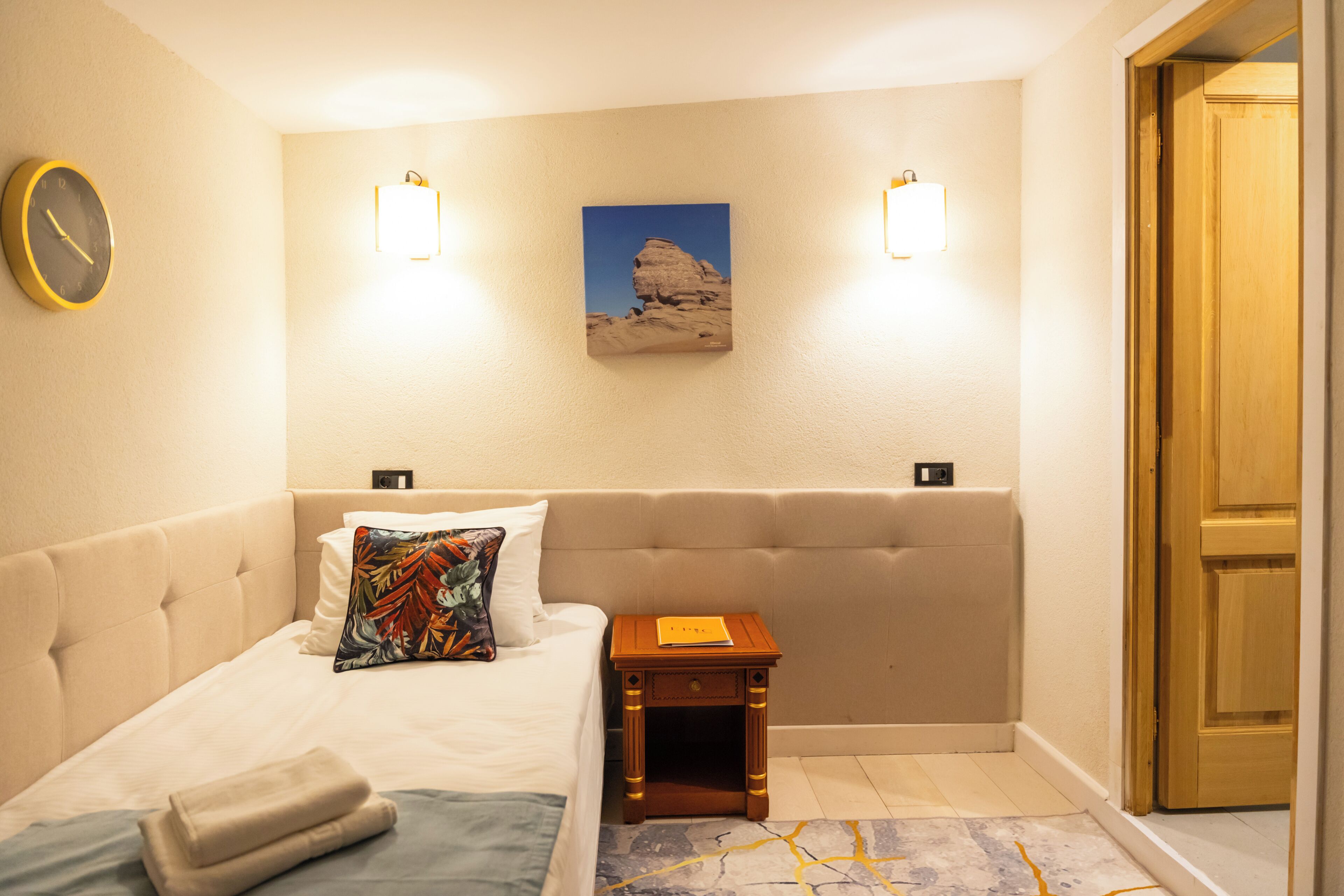 Une chambre d’hôtel avec un lit, une table de chevet, une horloge et un tableau au mur.