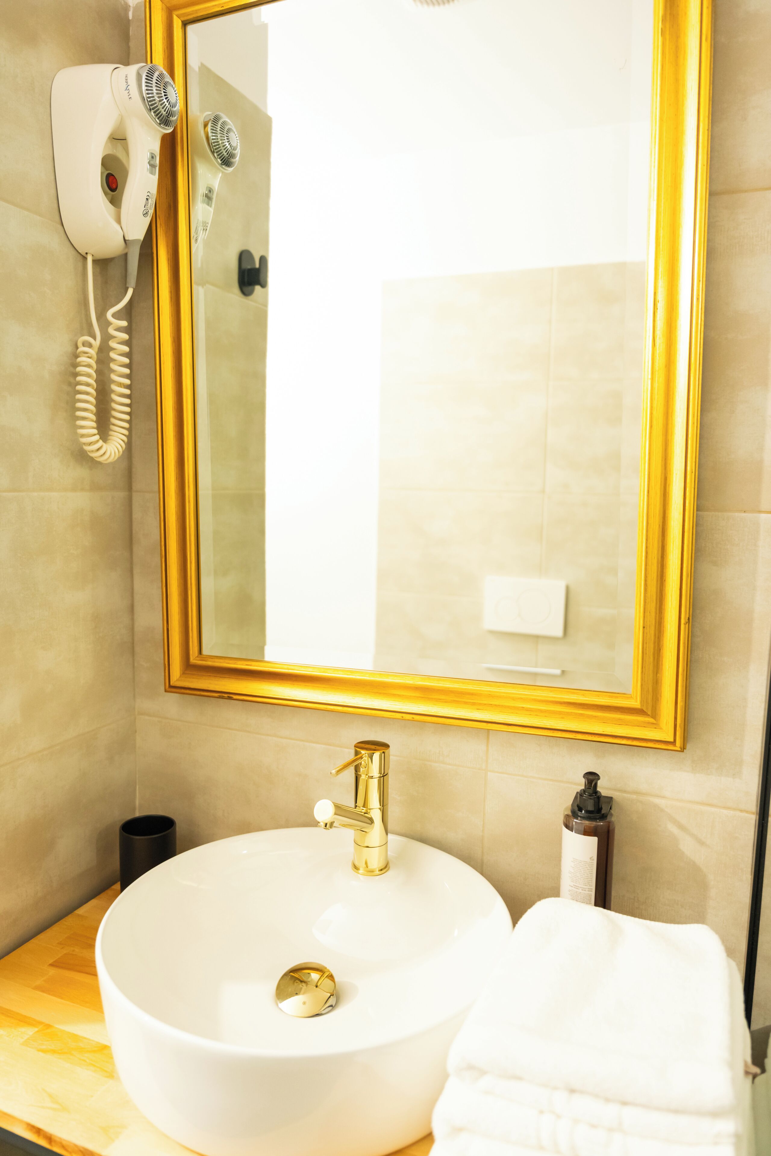 Ein Badezimmer mit einem weißen Waschbecken, einem goldenen Wasserhahn und einem spiegel mit goldener Rahmung.