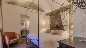 Ein Schlafzimmer mit Himmelbett, einer Wand aus Stein, Holzboden, Nachttisch und Sessel.