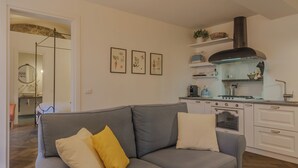 Ein modernes Wohnzimmer mit grauem Sofa, eine Küche mit weißen Schränken und einer schwarzen Dunstabzugshaube.