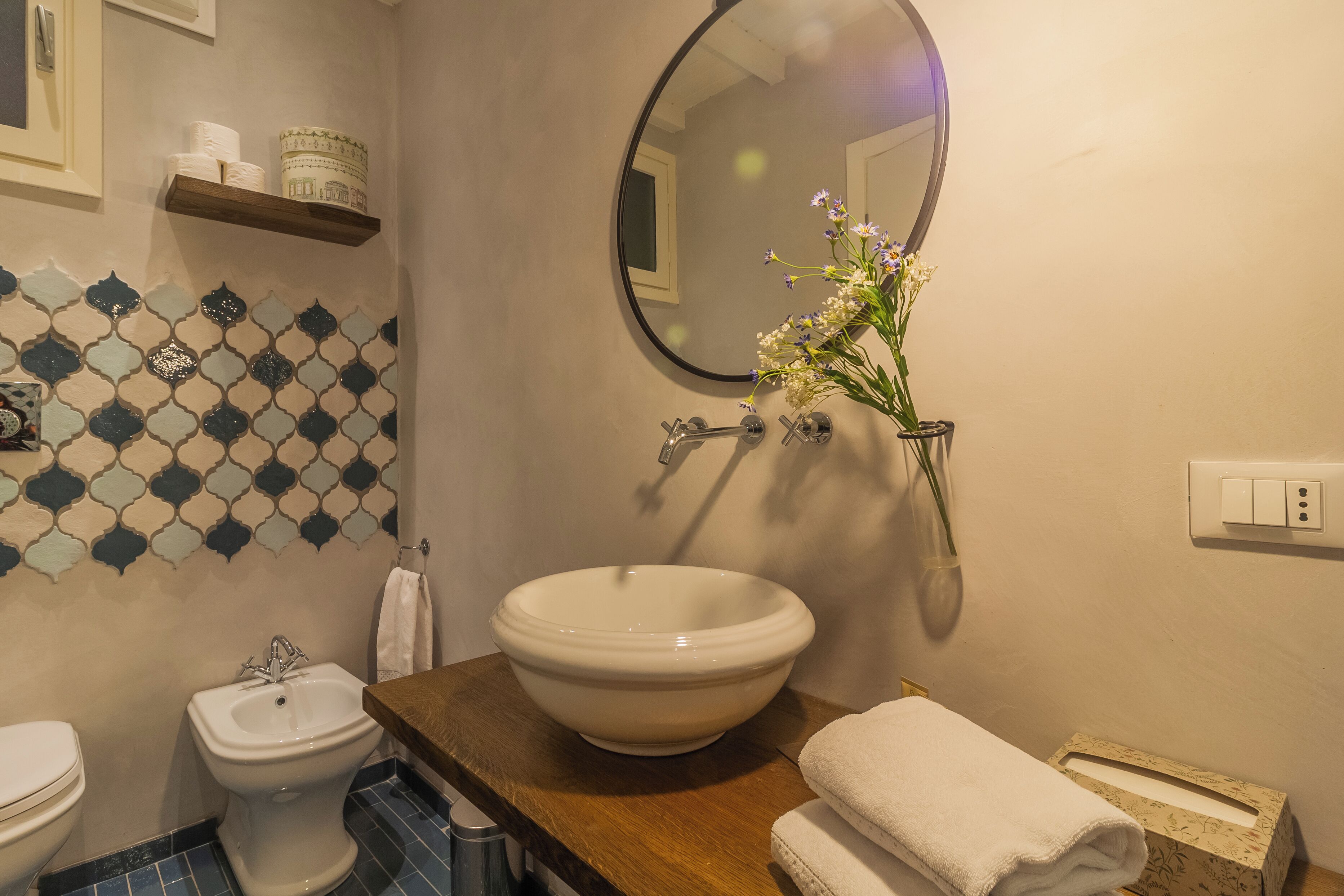 Une salle de bain avec un lavabo blanc, un bidet, un miroir, une serviette et un pare-chocs en carreaux à motifs.