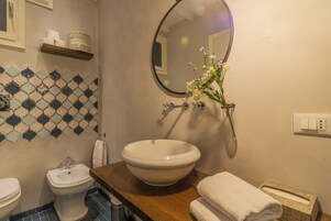 A bathroom with a white sink, a bidet, a mirror, a towel, and a patterned tile backsplash.