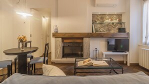 Ein modernes Wohnzimmer mit Kamin, einem Esstisch mit Stühlen, einer Couch, einem Glastisch und einem Fernseher.