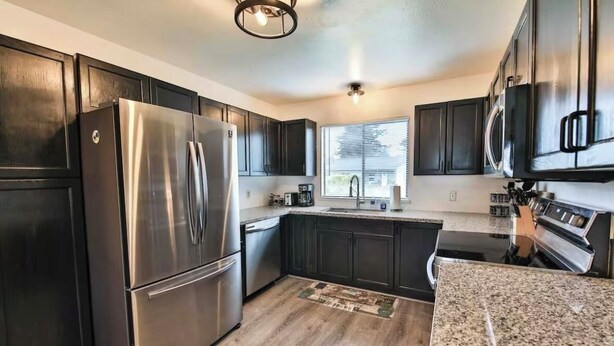 A modern kitchen with dark cabinetry, stainless steel appliances, and a granite countertop.