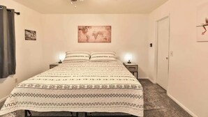 A bedroom with a bed, a ceiling fan, a world map on the wall, and a door.