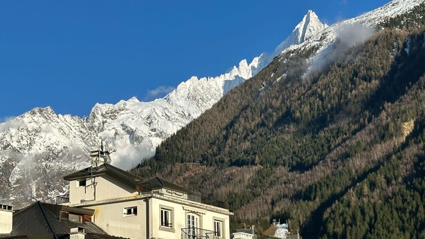 A mountain village with traditional architecture, snow-capped peaks, and a clear blue sky.