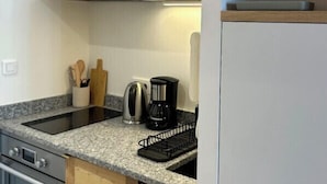 A compact kitchen with white cabinets, a granite countertop, a coffee maker, and a kettle.