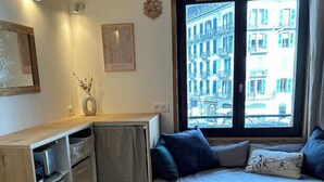 A cozy room with a dining table set for two, a built-in bench with cushions, and a window offering a view of buildings.