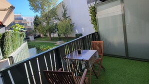 A balcony with a table and chairs, a view of buildings and trees, and a green artificial turf floor.