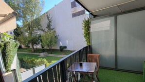 A balcony with a table and chairs, green artificial grass, and a view of a garden and buildings.