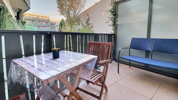 A balcony with a table and chairs, a bench, and a view of buildings and trees.