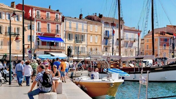 A bustling waterfront with colorful buildings, a docked boat, and people walking along the promenade.