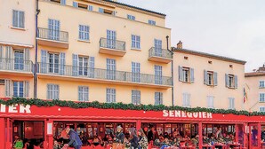 A red outdoor seating area of a restaurant with tables and chairs, and a building with balconies in the background.
