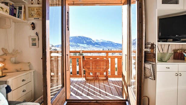 A wooden deck with a bench, a view of snow-capped mountains, and a white interior with shelves and a television. - Étoile Front de Neige (Demi-Quartier)