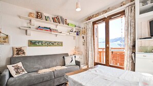 A cozy room with a grey sofa, a small table, and a bookshelf filled with books and decorative items. - Étoile Front de Neige (Demi-Quartier)