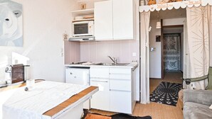 A compact kitchen with white cabinets, a microwave, and a sink. There is a dining table with a white tablecloth and a small glass. - Étoile Front de Neige (Demi-Quartier)