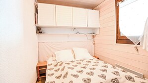 A small, cozy bedroom with a bed, a shelf above the bed, and a window with curtains. - Étoile Front de Neige (Demi-Quartier)