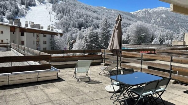 A balcony with a table and chairs, overlooking a snow-covered mountain. - Mountain Apartment With Terrace (Saint-Chaffrey)