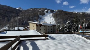 A snow-covered ski resort with a wooden fence, a building with multiple windows, and a mountain in the background. - Mountain Apartment With Terrace (Saint-Chaffrey)