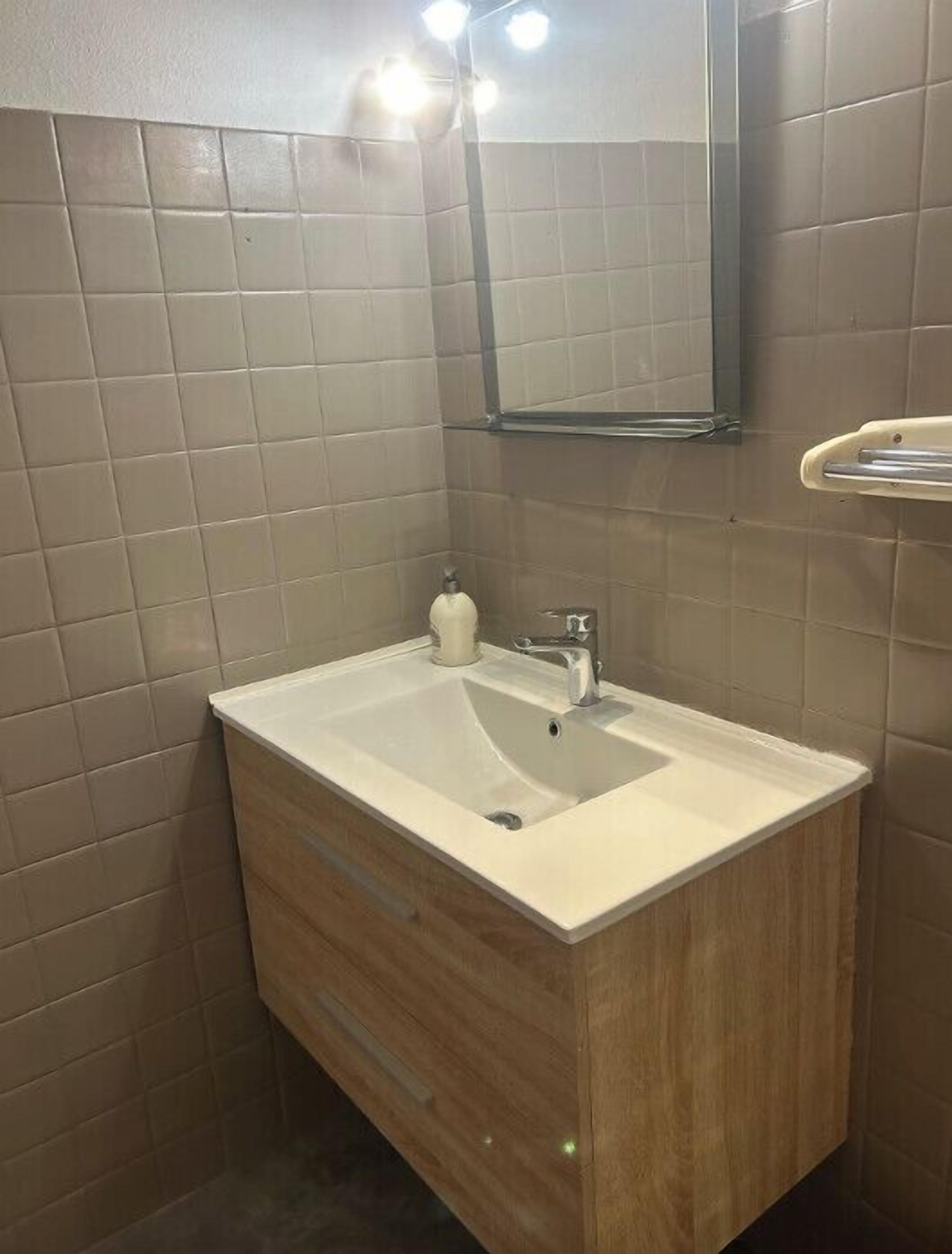 Un baño con tocador de madera, un lavabo blanco y un espejo encima.