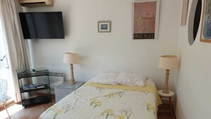 Ein Schlafzimmer mit einem Bett, zwei Nachttischlampen, einem an der Wand montierten Fernseher und einer kleinen Schrankwand.