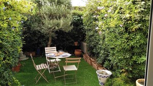 Ein kleiner, umzäunter Garten mit Tisch und Stühlen, umgeben von üppigem Grün und Topfpflanzen.