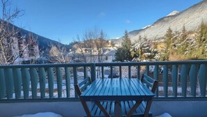 A balcony with a table and chairs, overlooking a snowy landscape with mountains and buildings.