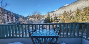 Un balcon avec une table et des chaises, donnant sur un paysage enneigé avec des montagnes et des bâtiments.