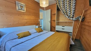A wooden room with a bed, a bedside table, a mirror, and a wardrobe.