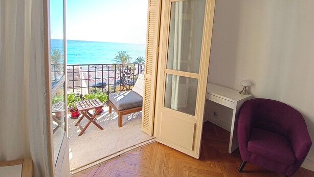 A room with a wooden floor, a purple chair, a white desk, and a view of the sea through a glass door. - Bright T3 - near the beach (Nice)