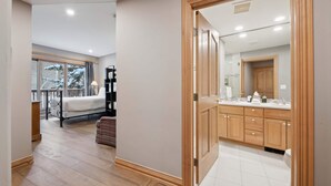 A modern hotel room with a wooden floor, a large bed, a small table, and a window with a view of a snowy landscape.