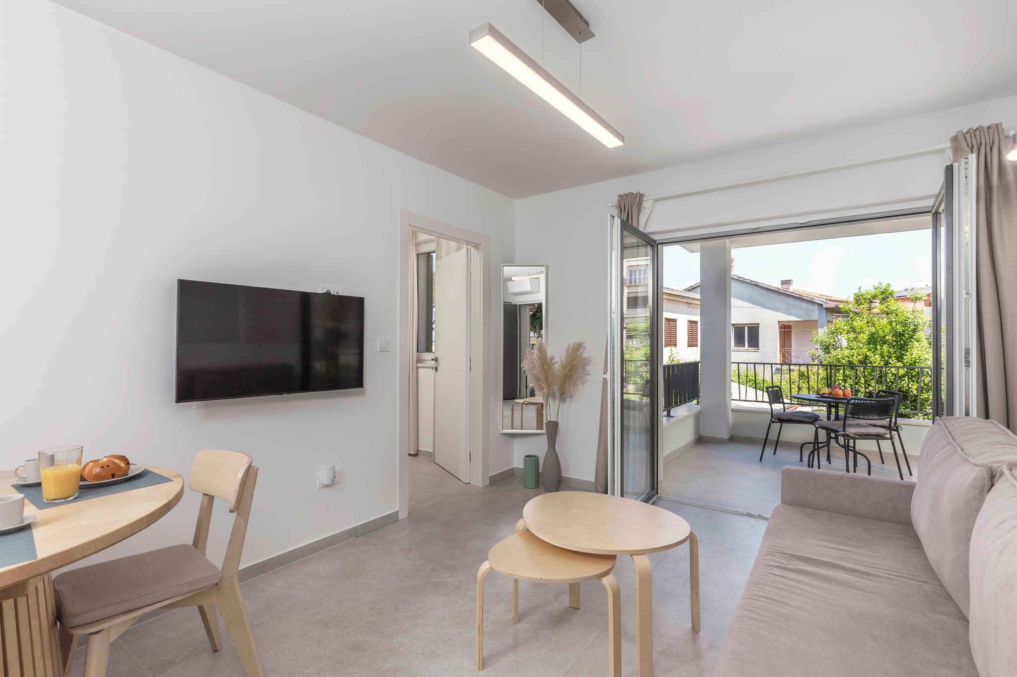 A modern living room with a flat-screen TV, a dining area with a table and chairs, a sofa, and a balcony with a table and chairs.