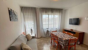 A living room with a sofa, dining table, chairs, a TV, and a patterned floor. - Holiday apartment with internet and balcony (Bibione)