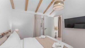 Una habitación de hotel con una cama, un televisor montado en la pared y techo de madera.