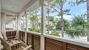 A covered outdoor seating area with wooden furniture and a view of a pool and trees. - Pickleball Courts, 30A, Pools, Beach Accesses (Santa Rosa Beach)