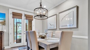 A dining area with a wooden table, beige upholstered chairs, and a chandelier. - Pickleball Courts, 30A, Pools, Beach Accesses (Santa Rosa Beach)