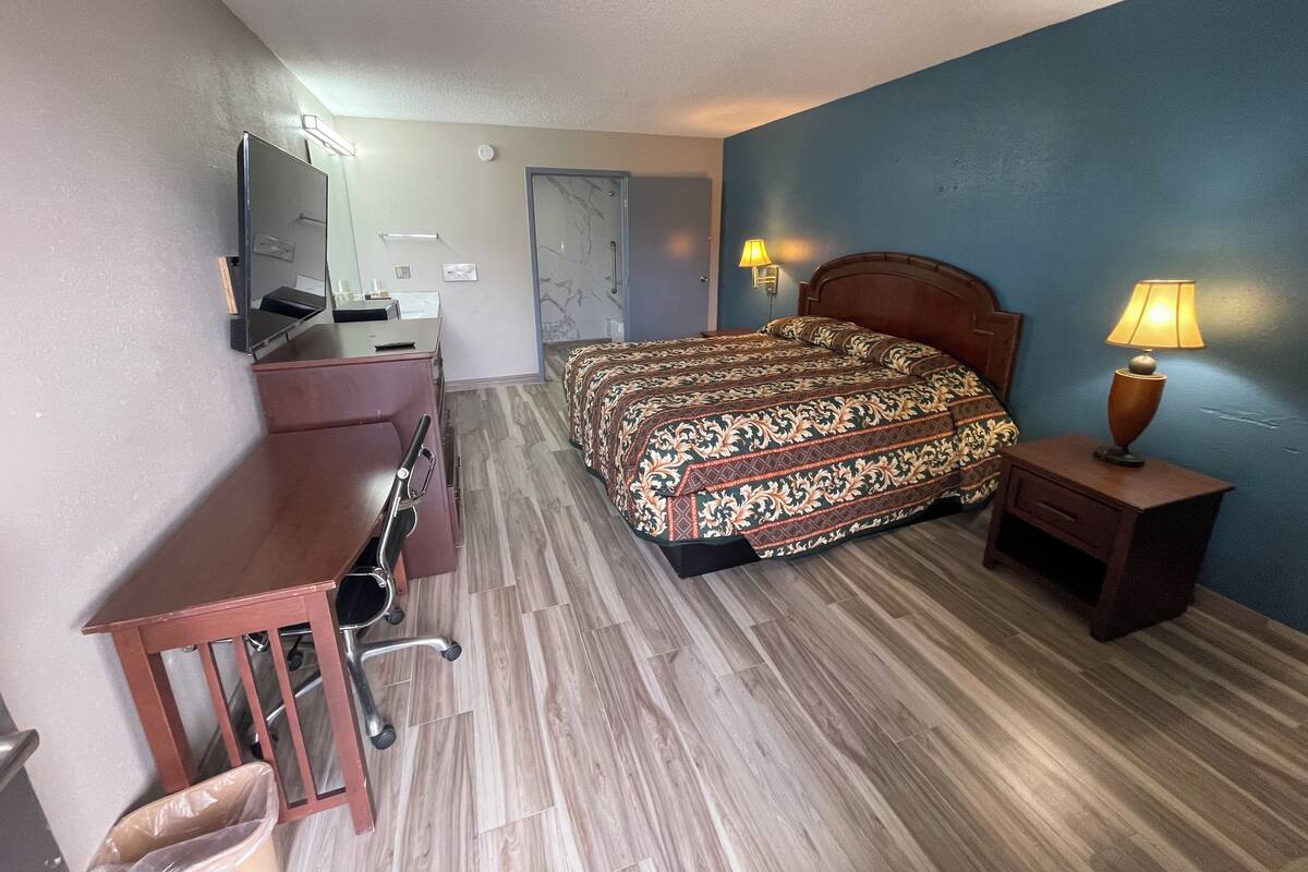 A hotel room with a bed, desk, chair, and a lamp.