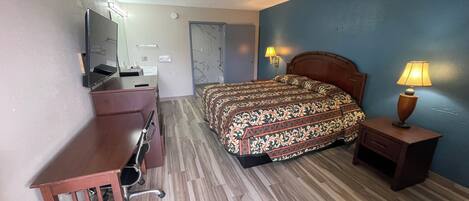 A hotel room with a bed, desk, chair, and a lamp.