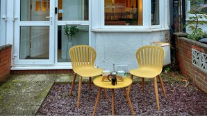 A house with a bay window, a satellite dish, and a small patio with two chairs and a table. - Stylish cottage in vibrant riverside village (North Ferriby)