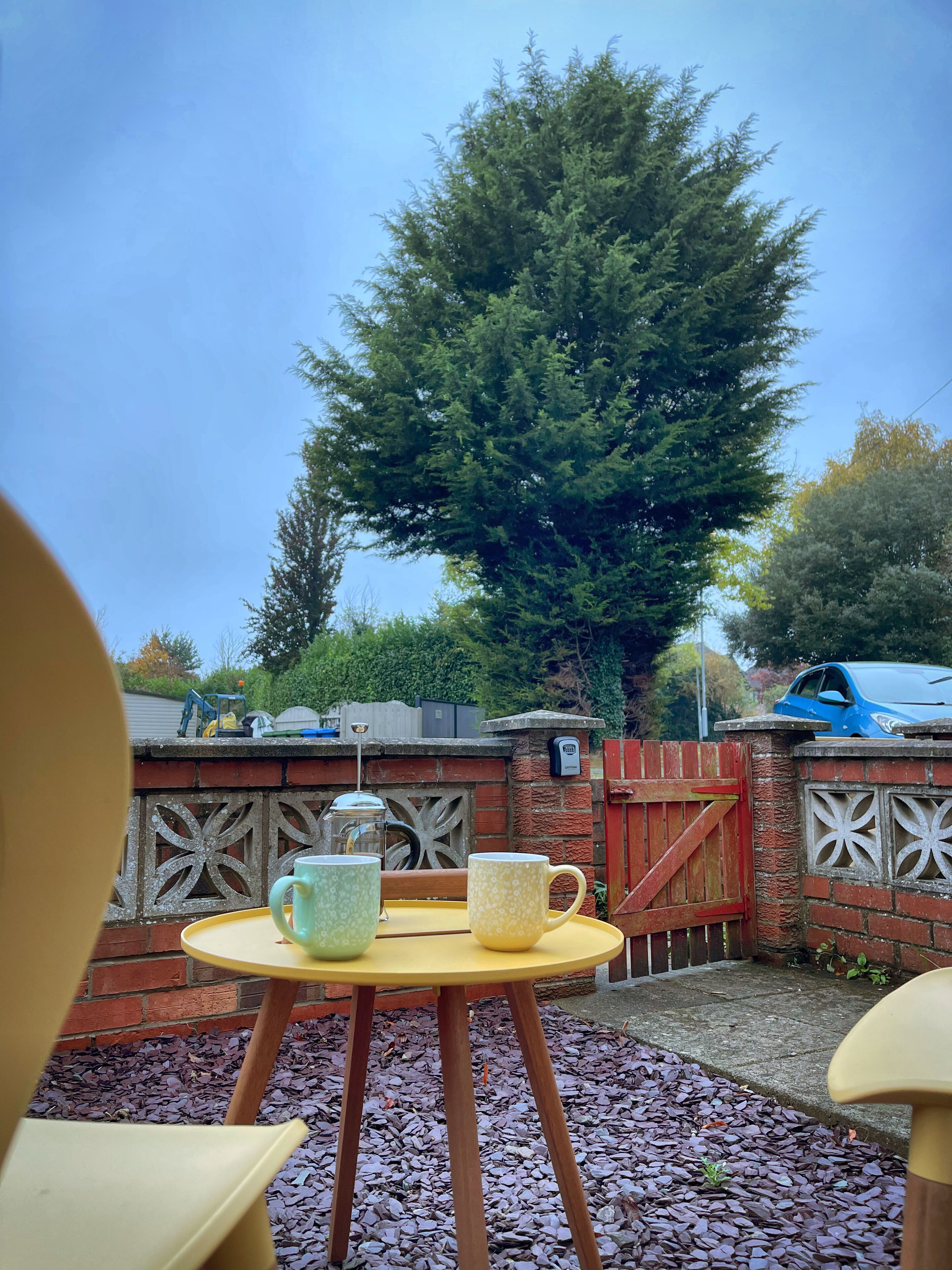 Eine Terrasse mit einem runden Tisch, zwei gemusterten Tassen und einer Kaffeekanne.