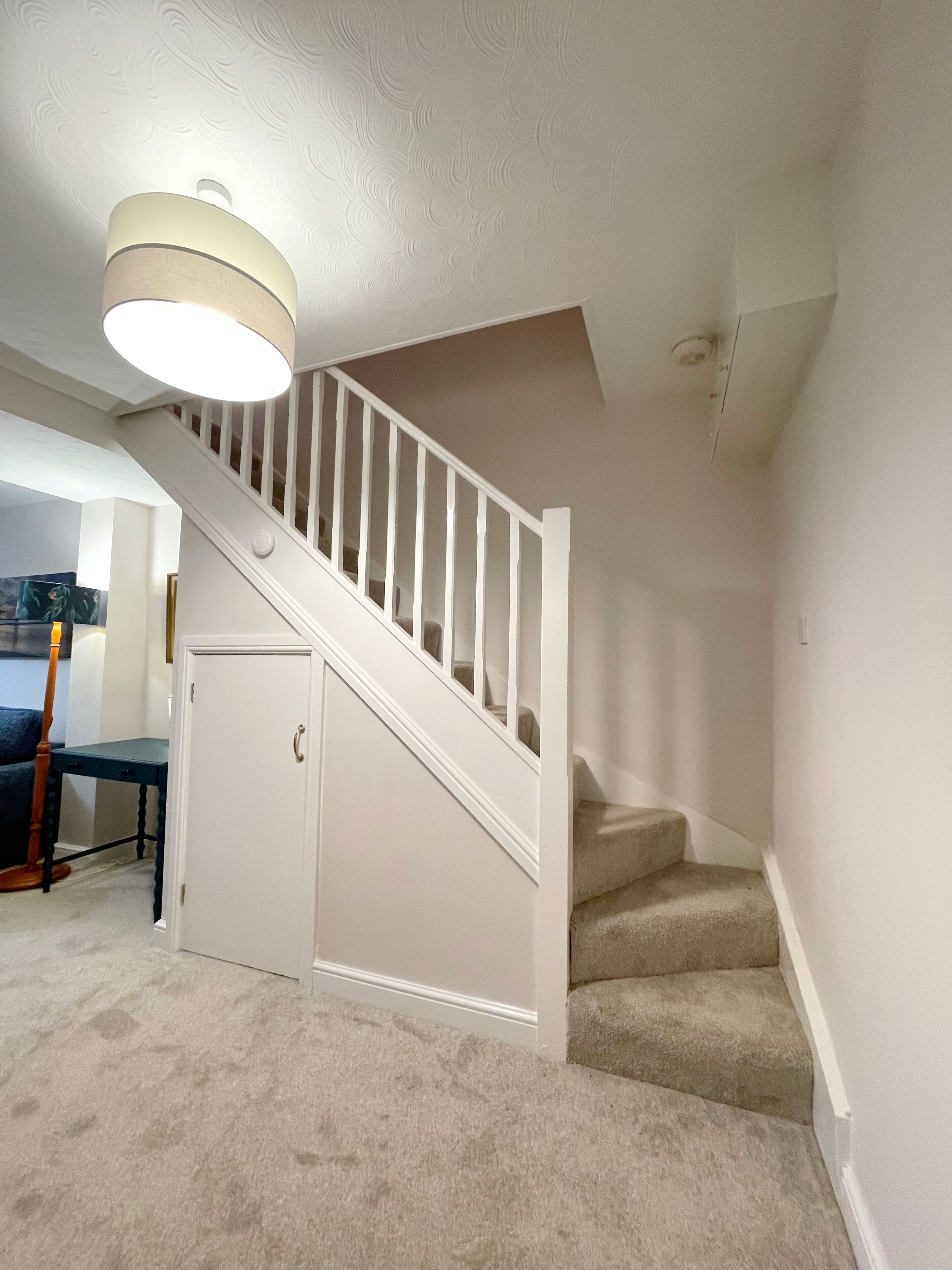 A staircase with a white railing, carpeted steps, and a light fixture above.