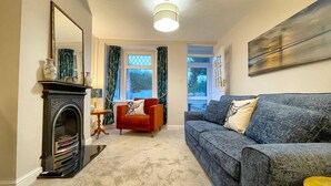 A living room with a fireplace, a sofa, a red armchair, and a painting on the wall. - Stylish cottage in vibrant riverside village (North Ferriby)