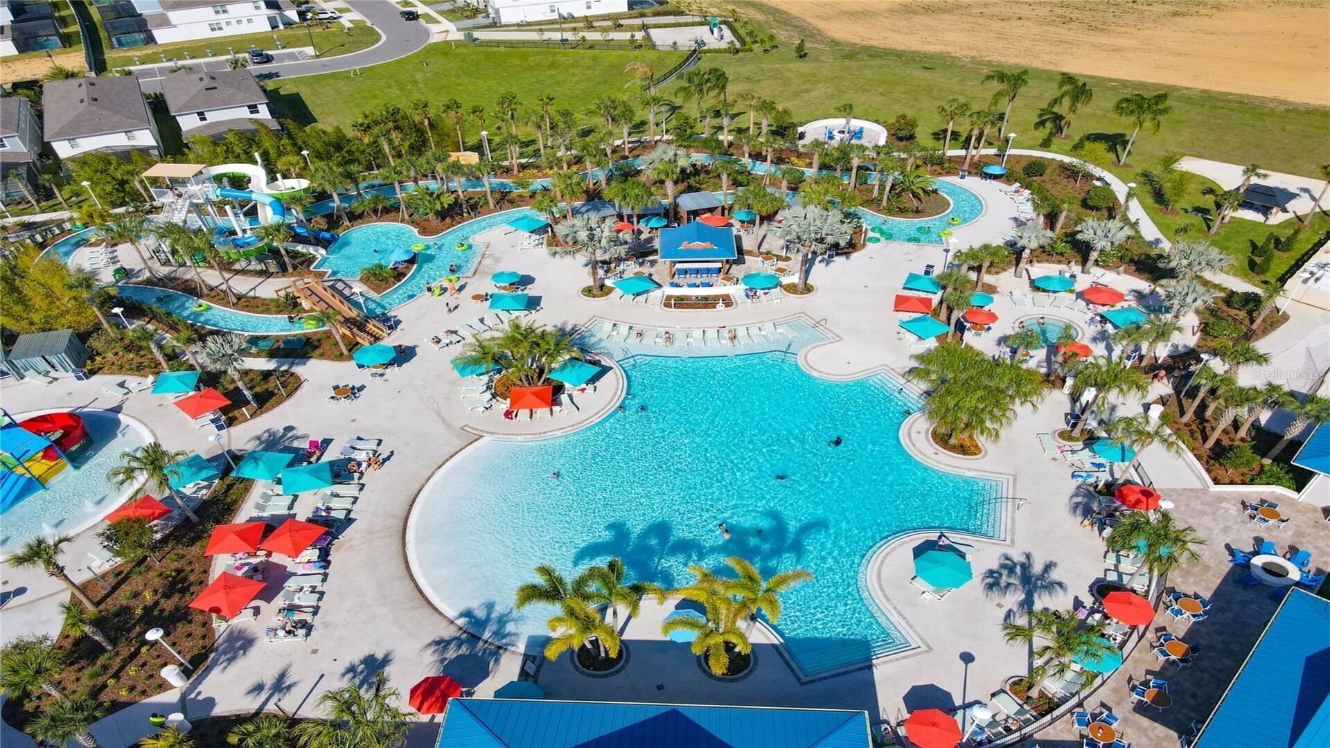 An aerial view of a resort with multiple swimming pools, sun loungers, and palm trees.
