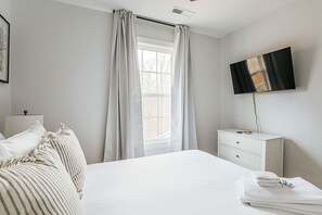 A bedroom with a bed, a TV, a window with curtains, a bedside table, and a dresser.